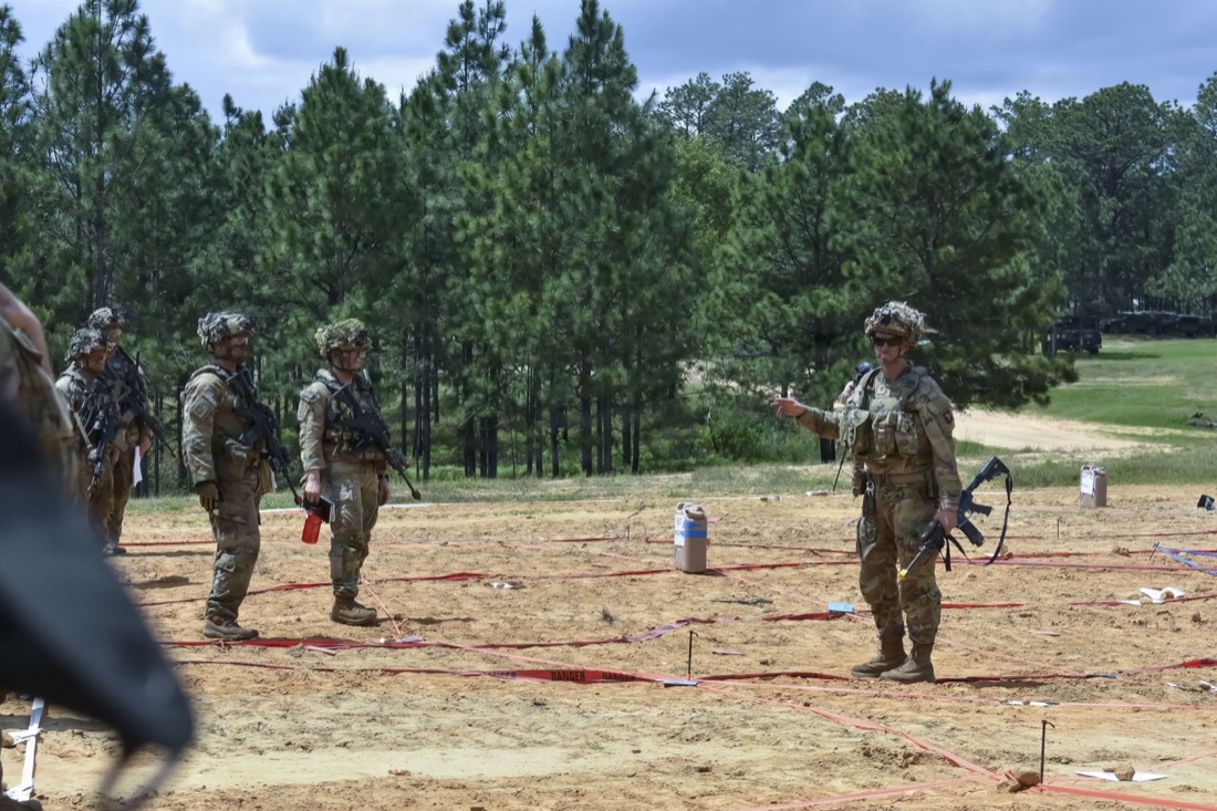 Soldiers in combat gear during a field training exercise, with an officer gesturing while giving directions near a marked range area.